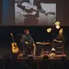 Musiker Odd Nordstoga og journalist Mona B. Riise sitter på scenen i Odda kino og snakker sammen. Ved siden av Odd står en gitar. Foto.